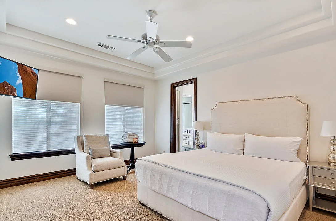 Spacious luxury master bedroom with king bed, ceiling fan, armchair and en-suite bathroom
